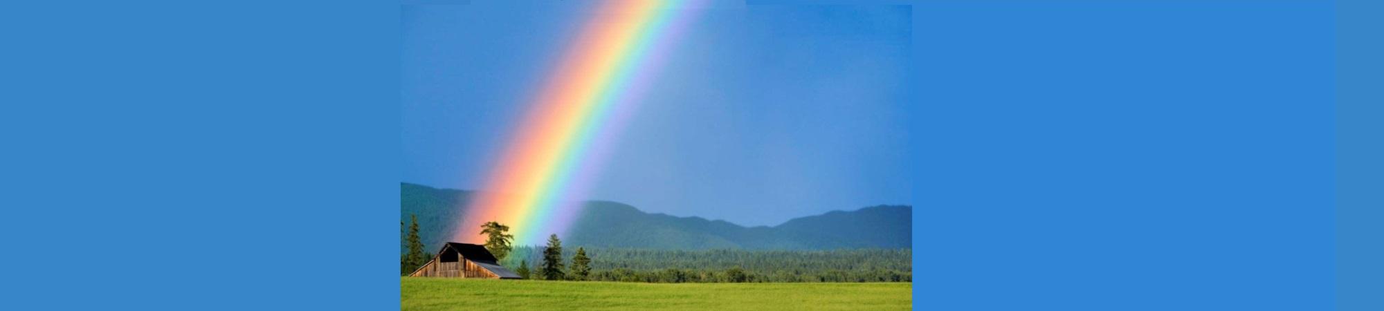 A beautiful rainbow behind an old barn. Blue sky, green grass. 